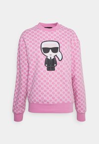 Roze sweatshirt met een herhalend patroon en een cartoonfiguur in zwarte zonnebril middenop. Geribbelde manchetten en zoom. Zachte textuur.