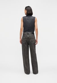 Αμάνικη μπλούζα από τζιν σε σκούρο γκρι ύφασμα, συνδυασμένη με ψηλόμεσα, φαρδιά γκρι τζιν παντελόνια με πίσω τσέπες και ραφές λεπτομέρειας.