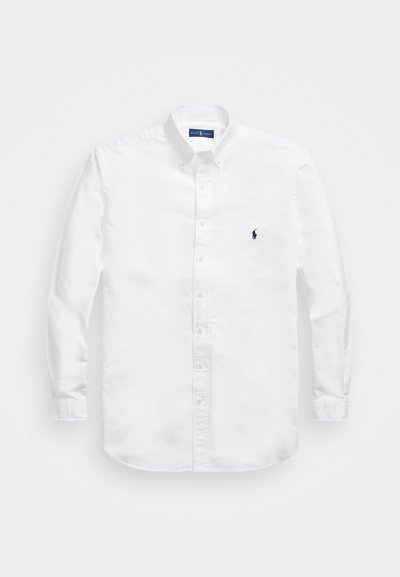 Λευκό πουκάμισο με μακρύ μανίκι και κουμπάκια από βαμβάκι, με μυτερό γιακά. Διαθέτει μικρό ναυτικό λογότυπο στο αριστερό μέρος του στήθους και κουμπιά στους καρπούς.