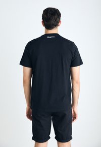 Svart t-shirt i bomull med korta ärmar, rund halsringning och en logotyp på baksidan. Matchas med svarta shorts, båda i enfärgat material.