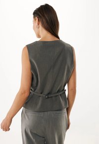 Ärmlös grå blus med en subtil vertikal textur, med ett knytbälte i midjan och en rund halsringning.