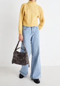 Pull à col roulé en maille torsadée jaune, jeans larges bleu clair et sac à main en cuir gris avec une bandoulière robuste. Chaussures plateforme noires.