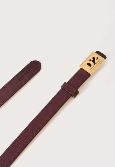 Ceinture en cuir brun foncé avec une boucle rectangulaire dorée gravée des lettres D et Z sur un fond uni clair.