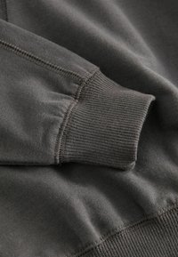 Manche de sweatshirt grise avec un poignet côtelé, texture de tissu lisse et détails de coutures contrastés. La vue rapprochée met en avant la construction.