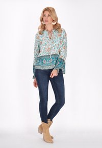 Bluză florală de culoare bleu deschis, cu mâneci volănaș, guler cu șnur și un bandou cu model turcoaz, asortată cu blugi skinny închis la culoare și botine bej.