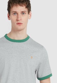 T-shirt grigia a maniche corte, colletto e polsini a coste verdi. Piccolo logo arancione sul petto. Texture del tessuto liscia.