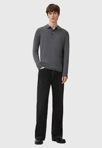 Polo a maniche lunghe grigio scuro con colletto, abbinato a jeans neri a gamba larga. Il tessuto sembra liscio e leggero.