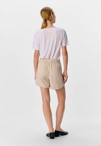 Beige shortsd med elastisk talje, parret med en lysegrå T-shirt. Outfitet har en afslappet pasform og minimalistisk design. Sorte sko.
