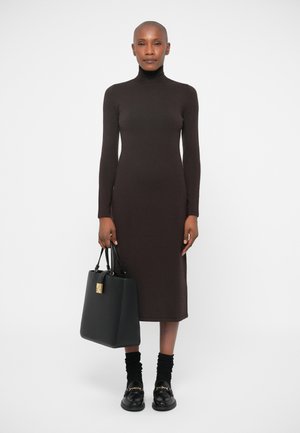 Robe turtleneck marron à manches longues avec une silhouette ajustée. Associée à un sac à main noir avec des accessoires en or et des mocassins noirs avec une chaîne.
