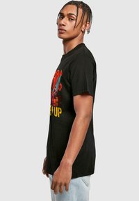 Black cotton T-shirt with short sleeves, featuring a colorful graphic print and text on the front, modeled on a person facing sideways.