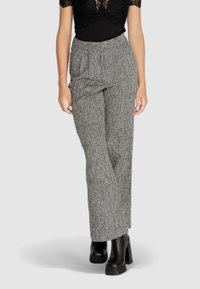 Pantaloni larghi grigi, con texture e pleats frontali, a vita alta. Abbinati a stivaletti neri con zeppa, indossati con un top in pizzo nero.