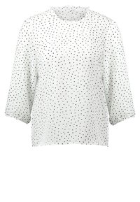 Blouse blanche à pois noirs, col rond et manches trois-quarts. Tissu léger et transparent avec une texture douce et un col à volants.