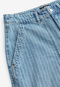 Pantalones cortos de mezclilla azul claro con rayas verticales, que cuentan con un cierre de botón, cinturilla con lazo y bolsillos laterales en ángulo. Detalle de tela texturizada visible.