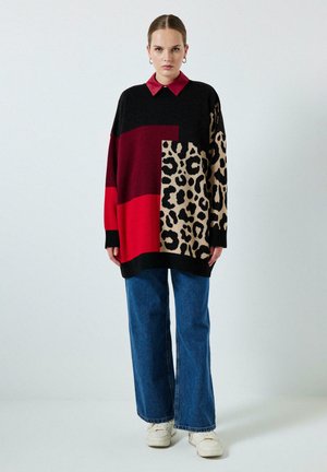 Maglione in maglia over-size con motivi neri, rossi e a stampa leopardata; presenta un collo rosso. Abbinato a jeans in denim a gamba larga.