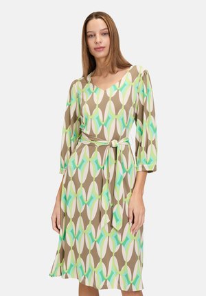 Robe marron avec un motif abstrait vert, blanc et turquoise. Présente un décolleté en V, des manches 3/4 et une taille ceinturée. Tissu lisse.