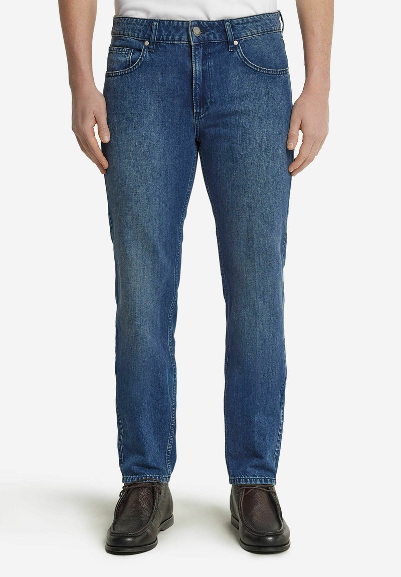 Blå denimjeans med rak passform, femfickorsdesign, metallknapp och nitar, samt subtila blekningar. Bärs med svarta skor.