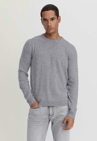 Grau melierter Rundhalspullover aus weichem, strukturiertem Stoff mit gerippten Bündchen und Saum, kombiniert mit hellgrauen Jeans für einen stimmigen Look.