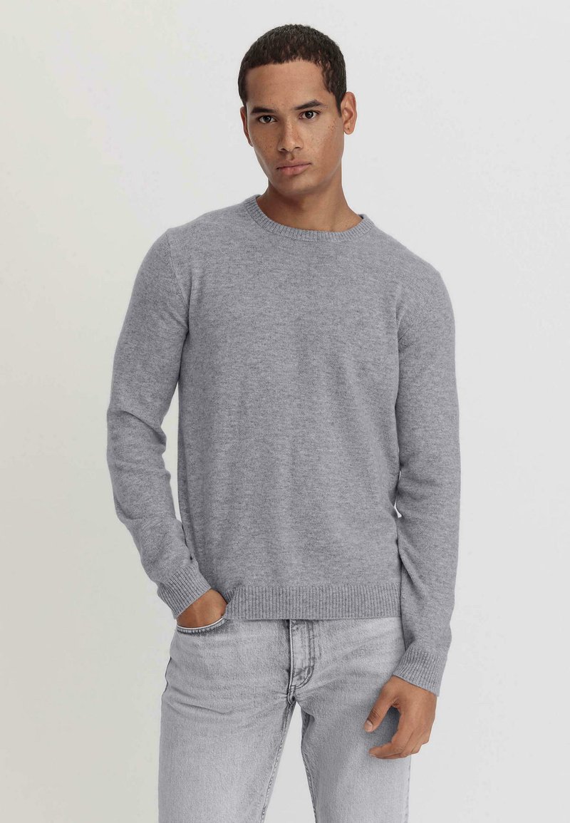 Grau melierter Rundhalspullover aus weichem, strukturiertem Stoff mit gerippten Bündchen und Saum, kombiniert mit hellgrauen Jeans für einen stimmigen Look.