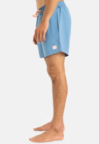 Blue swim shorts with an elastic waistband and pink drawstring. Features a small pink logo patch on the left leg and a smooth texture.