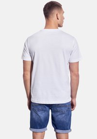 Vit bomullst-shirt med korta ärmar, klassisk rundhalsdesign. Bärs ihop med blå denimshorts med uppvikta benslut och bakfickor.