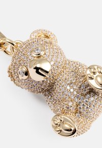 Ciondolo a forma di orsacchiotto d'oro, impreziosito da strass, con un viso e zampette d'oro lucido. La sua forma arrotondata e la superficie texturizzata creano un interesse visivo.