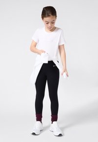 Witte katoenen t-shirt met reliëf "Champion" logo, zwarte leggings, witte sport schoenen en bordeauxrode crew sokken. Witte trui om de taille geknoopt.