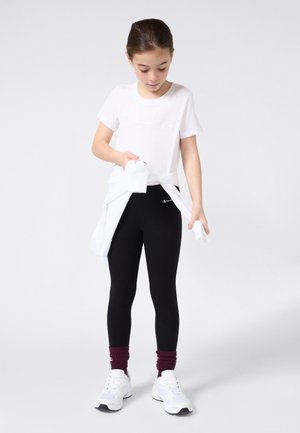 Camiseta de algodón blanca con el logo "Champion" en relieve, leggings negros, zapatillas deportivas blancas y calcetines de tripulación en color burdeos. Suéter blanco anudado a la cintura.