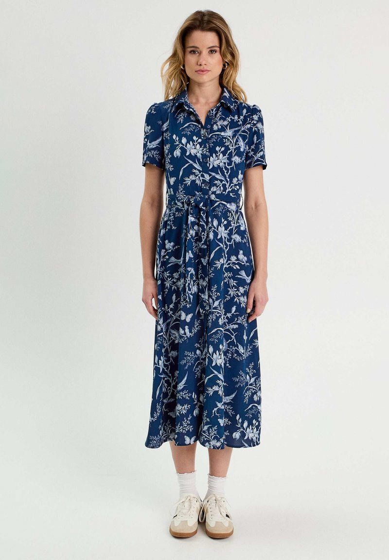 Navyblaues Blumenmusterkleid mit kurzen Ärmeln, einem kragenbesetzten Ausschnitt und einem taillierten Gürtel. Es hat eine fließende Silhouette und einen leichten, strukturierten Stoff.