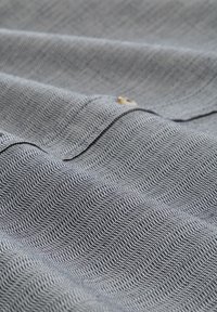 Tissu texturé avec un motif en chevrons dans des nuances de gris, comportant de fines lignes et un petit détail de bouton le long du bord.