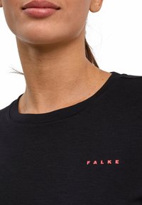 Zwart shirt met korte mouwen en een ronde hals, met een contrasterend roze "FALKE"-logo aan de linkerkant van de borst.