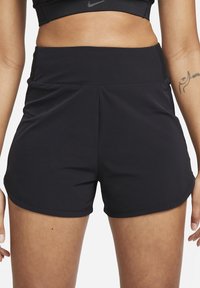 Acercamiento de una persona que lleva pantalones cortos deportivos negros de cintura alta y un sujetador deportivo negro, mostrando un tatuaje en el brazo derecho.