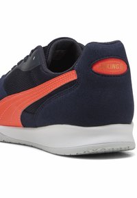 Zapatilla azul marino con acentos naranjas, materiales de gamuza y malla, forma redondeada y una suela blanca texturizada con la marca "KING" en el talón.