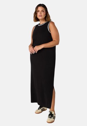 Schwarzes, ärmelloses Maxikleid mit seitlichen Schlitzen, ausgestattet mit einem kontrastierenden gerippten Halsauschnitt; kombiniert mit beigen Sneakers mit schwarzen Schnürsenkeln.