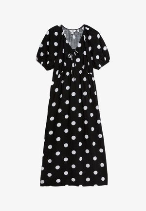 Czarna sukienka w białe kropki, z dekoltem w kształcie litery V, krótkimi bufkami i szczegółem ze sznurkiem z przodu. Lekki materiał.