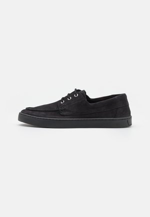 Chaussures noires en daim à lacets avec semelle en caoutchouc, présentant un bout rond et des détails de couture minimalistes. Texture lisse sur l'ensemble.