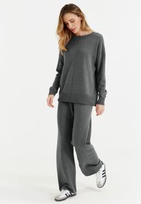 Pull gris et pantalon large assorti en tissu doux. Le pull a un col rond et des poignets côtelés. Chaussures de sport décontractées.