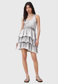 Vestido gris de capas con bordes deshilachados, diseño sin mangas y cuello redondo. Complementado con sandalias metálicas de tiras.
