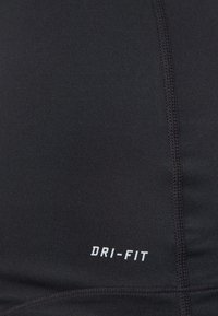 Zwarte sporttop van glad, rekbaar materiaal met zichtbare naden. "DRI-FIT" logo in het wit nabij de onderkant.