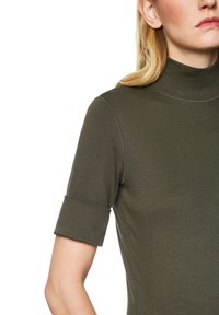 Olive green fitted top with a high collar and short, rolled sleeves. Features subtle texture and contrasting stitching details.