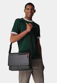 Schwarze Ledermessenger-Tasche mit Klappenverschluss, orangefarbenem Reißverschlussgriff und verstellbarem Tragegurt. Glatte Oberfläche und rechteckige Form.