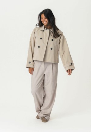 Beige cropped Jacke mit doppelt geknöpften schwarzen Knöpfen, weiten Ärmeln und passenden hellgrauen Weitbein-Hosen mit strukturierter Oberfläche.