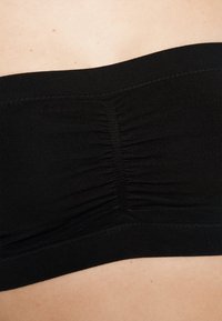 Μαύρο strapless μπαντό κορμάκι φτιαγμένο από ελαστικό ύφασμα, με συγκεντρωμένες λεπτομέρειες στο κέντρο και λείο, ελαστικό λουρί στις άκρες.