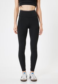 Zwarte high-waisted legging gemaakt van rekbaar materiaal, met een gladde textuur en een nauwsluitend ontwerp, gecombineerd met witte sneakers.