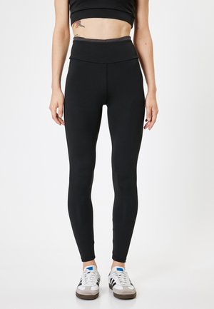 Zwarte high-waisted legging gemaakt van rekbaar materiaal, met een gladde textuur en een nauwsluitend ontwerp, gecombineerd met witte sneakers.