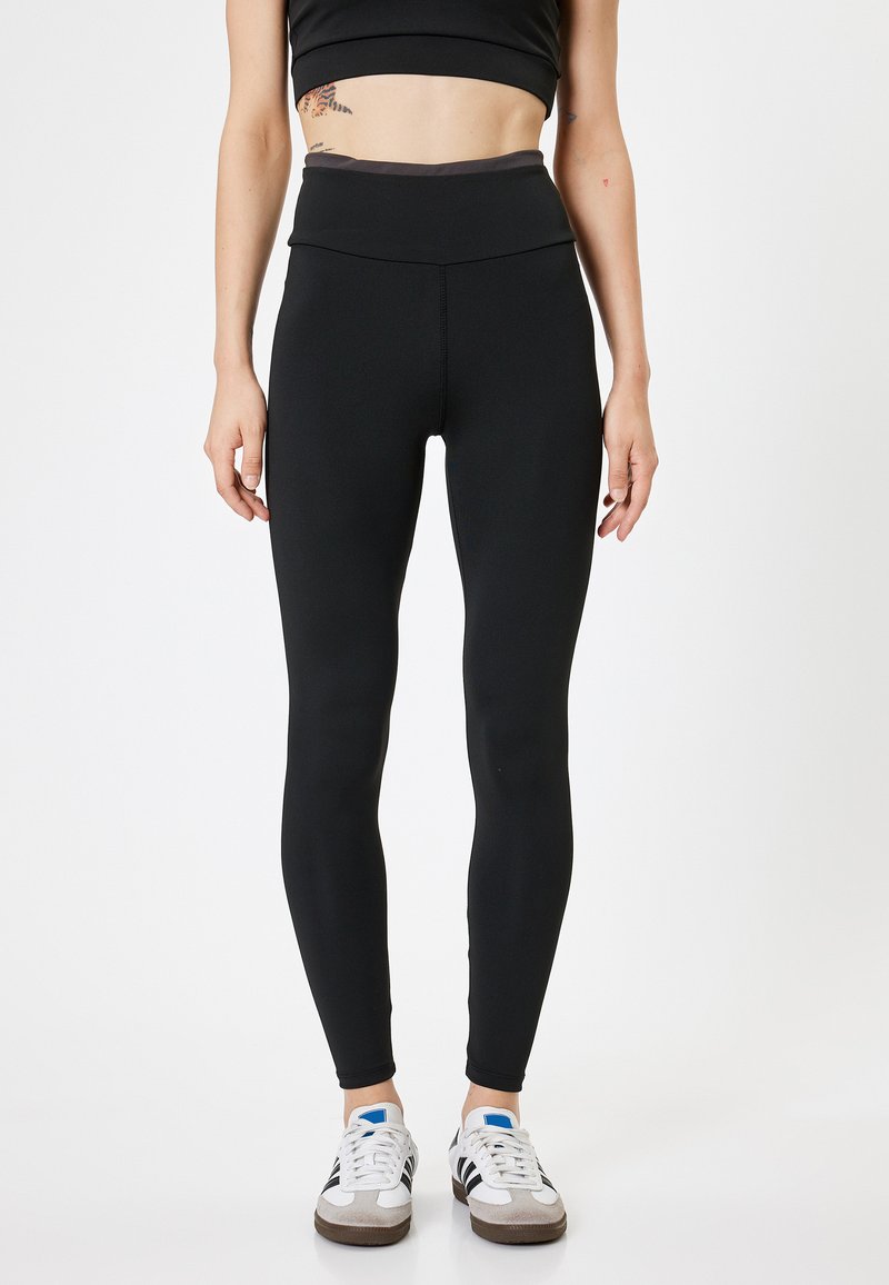 Zwarte high-waisted legging gemaakt van rekbaar materiaal, met een gladde textuur en een nauwsluitend ontwerp, gecombineerd met witte sneakers.