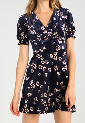 Mini-robe en velours bleu marine à imprimé floral blanc et rose, manches bouffantes, encolure en V et détail froncé au niveau de la poitrine.