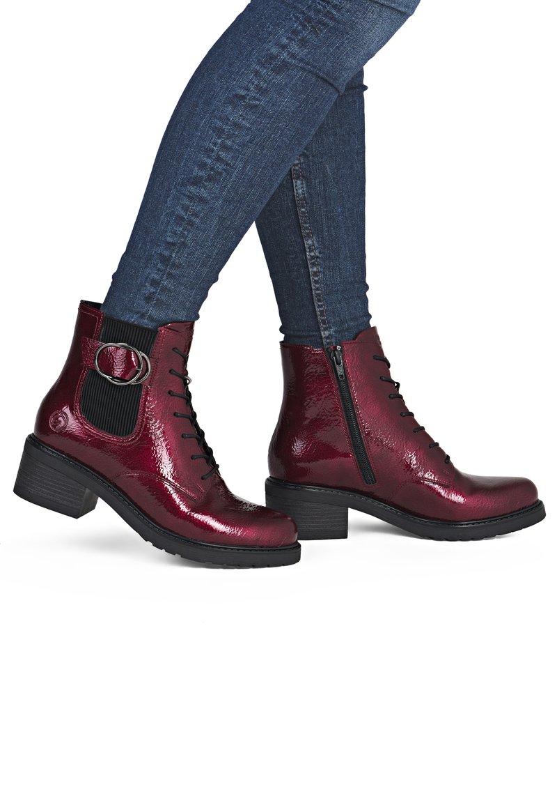 Bottines bordeaux à fini brillant, avec lacets, fermeture éclair latérale, panneau élastique et un accent métallique circulaire. Talon noir épais.