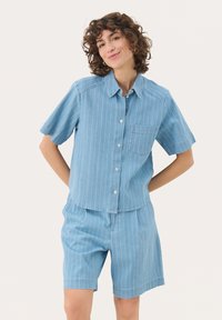 Helles blau gestreiftes Kurzarmhemd mit durchgehender Knopfleiste und Brusttasche, kombiniert mit passender Shorts aus ähnlichem Stoff und Muster.