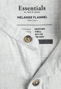 Essentials de Jack & Jones Chemise en flanelle mélangée avec tissu Heather Twill 100% coton et deux boutons visibles sur tissu gris clair.