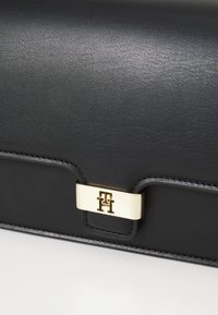 Svart skinnclutch med en jevn tekstur, med en gullfarget lås med preget logo. Elegant, rektangulært design med sømdetaljer.